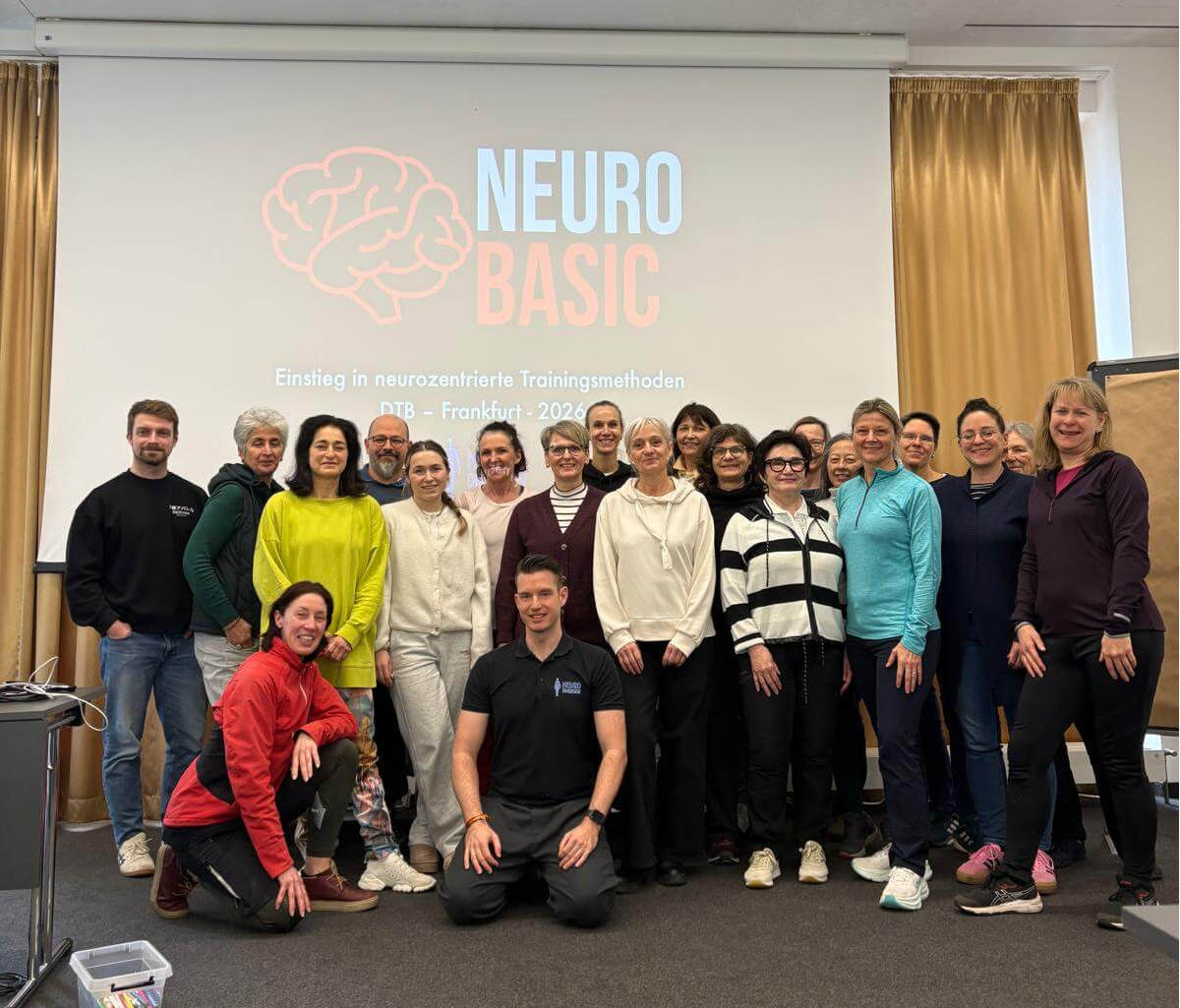 Teilnehmende einer Neuro-Basic-Schulung stehen vor einem Bildschirm mit Präsentationsfolie